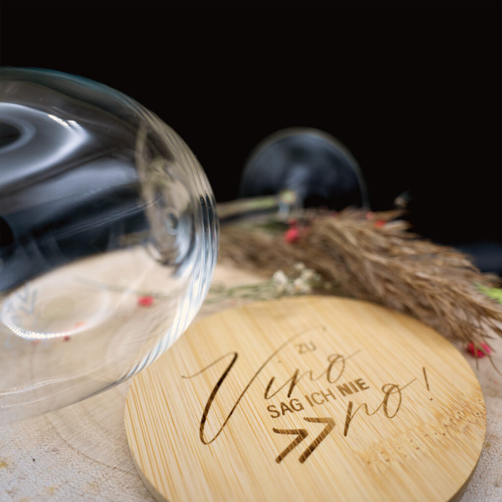 Arrangement Weinglas und Bambusuntersetzer belasert mit dem Spruch "Zu Vino sag ich nie no"